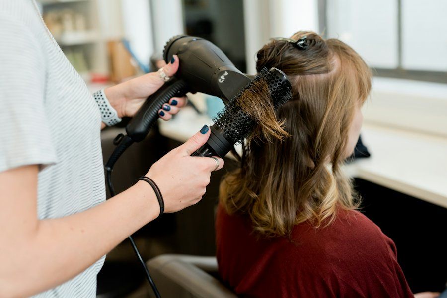 Penata rambut mengeringkan dan menata rambut klien dengan sisir bulat